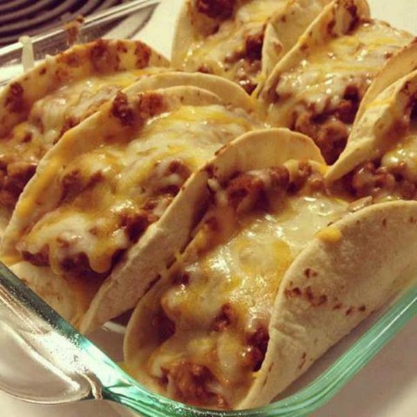 Close-up of cheesy soft tacos filled with ground meat, served in a glass baking dish.