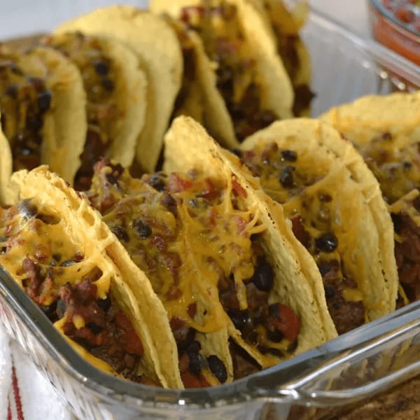 Baked tacos with melted cheese, black beans, and meat in a glass dish, with salsa in the background.